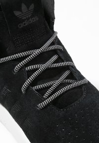 Baskets en daim noir avec un orteil perforé, semelle blanche contrastante et lacets noirs et blancs marbrés. Présente le logo Adidas sur la languette.