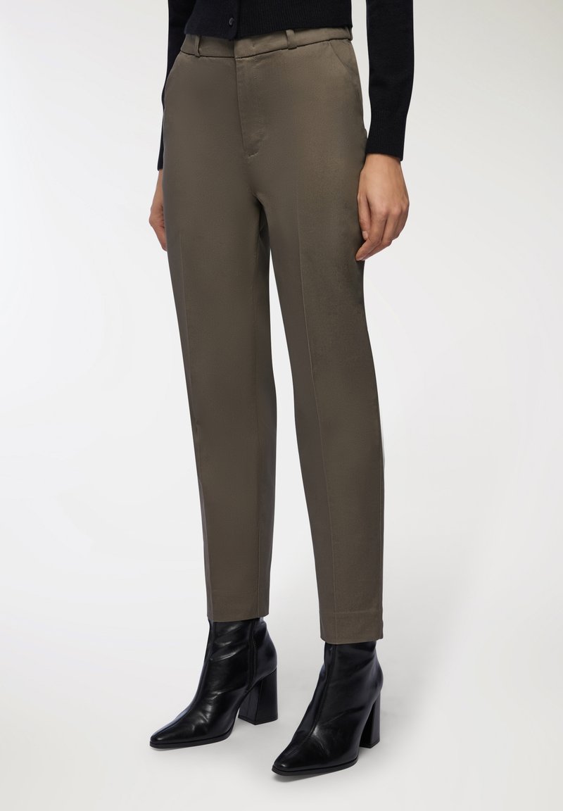 Pantaloni verdi oliva con un taglio su misura, caratterizzati da una texture liscia e una leggera lucentezza. Abbinati a stivaletti neri a punta.