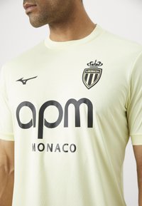 Svetložltý atletický dres s krátkymi rukávmi, s čiernym logom AS Monaco a textom "apm MONACO" v tučnom čiernom písmene.