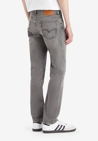 Grå denimjeans med rett snitt, med baklommer og et lærpatch på midjebåndet. Kombinert med hvite joggesko.