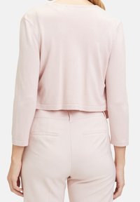 Světlé růžové krátké svetřík z měkké látky, s tříčtvrtečními rukávy a zaobleným zadním lemem. Kombinováno se světlými růžovými kalhotami.