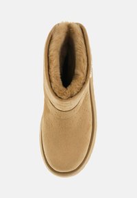 Stivaletto alla caviglia in suede tan con punta rotonda, morbida fodera in pelliccia e motivo floreale in rilievo. Presenta un tirante e suola in gomma piatta.