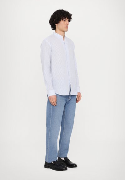 Skjorte med knapper i blå og hvite vertikale striper, mandarin-krage og lange ermer, kombinert med lyseblå rette jeans og svarte sko.
