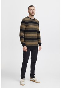 Maglione a righe marrone e nero, texture in maglia, scollo rotondo, jeans neri e sneaker bianche con dettagli marroni.