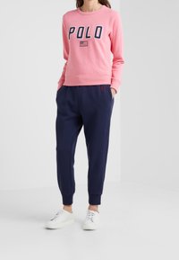Rosa sweatshirt med "POLO"-text och detalj av den amerikanska flaggan, kombinerad med marinblå joggerbyxor och vita sneakers. Avslappnad passform och i blandning av bomull.