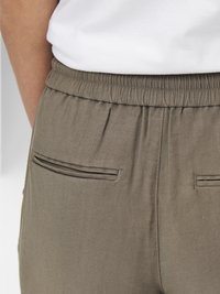 Pantalons olive à taille élastique avec deux poches arrière présentant des détails en surpiqûre. Le tissu est lisse avec un léger éclat, et le design est structuré.
