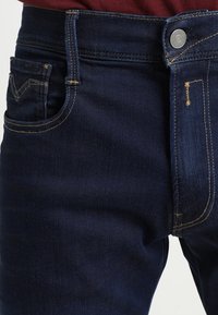 Mörkblå denimjeans med klassisk passform, framficka och synliga söm detaljer längs midjebandet och fickorna.