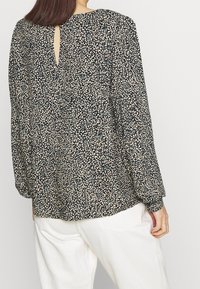 Schwarze Bluse mit floralem und blätterförmigem Muster in Creme und Blau, mit einem Schlüsselloch-Ausschnitt im Rücken, langen Ärmeln und entspannter Passform.