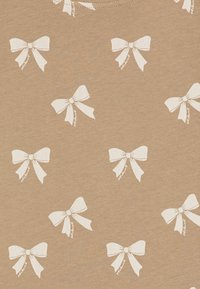 Light brown t-shirt featuring a repeated pattern of white bows. Soft texture, classic round neckline, and casual design.