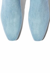 Zapatos de punta azul claro hechos de denim, con una textura suave y un diseño elegante, con una silueta plana y angular.