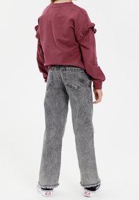 Bordeauxroter Sweatshirt mit Rüschensäumen, kombiniert mit grauen Jeans mit ausgefranstem Saum. Das Outfit wird mit schwarzen Sneakers abgerundet.