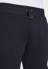 Černé bavlněné tepláky s elastickým pasem a stahovací šňůrou, hladkého povrchu. Bez viditelných kapes nebo vzorů.