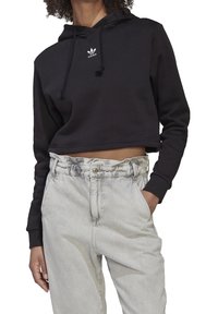 Svart avklippt hoodie med dragsnören och vit Adidas-logotyp. Matchas med ljusgrå högmidjade jeans med veckad midjeresår.