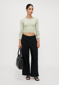 Light green cropped long-sleeve top, black wide-leg trousers, black handbag, and black strappy heeled sandals with studs.