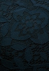 Mörkblått tyg med ett detaljerat blommönster i spets, med varierande texturer och öppna vävningar som framhäver intrikata designelement.