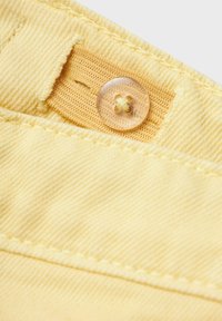 Tela amarilla con una textura estriada, que presenta un botón transparente y una etiqueta tejida. La costura es visible a lo largo de las costuras.