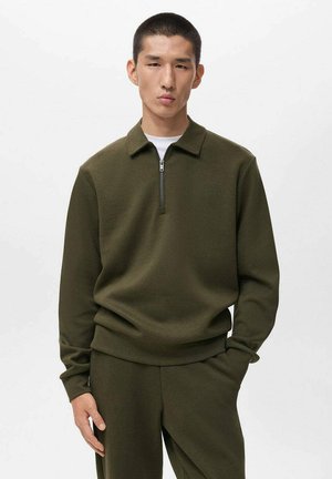 Sudadera verde oliva con cremallera y cuello tipo polo, con una textura suave y puños acanalados, acompañada de pantalones a juego en verde oliva.