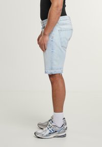 Világoskék farmer rövidnadrág, elhasználódott szegéllyel, deréknál viselve. Ezüst színű sportcipővel és fehér zoknikkal párosítva.