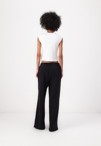 Top blanco sin mangas combinado con pantalones amplios negros. El top tiene un diseño ajustado, y los pantalones cuentan con una cintura elástica para mayor comodidad.