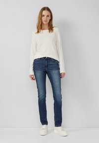 Haut à manches longues gris clair avec un décolleté carré, associé à un jean slim bleu foncé et des baskets blanches. Design simple, sans motifs visibles.