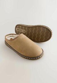 Beige slip-on slippers with soft fabric upper, faux fur lining, and contrasting braided trim. Textured rubber outsole for grip.