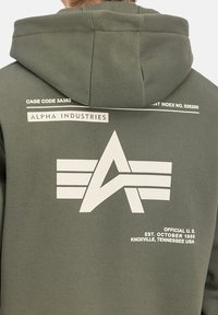Felpa di colore verde oliva con un grande logo bianco che presenta una "A" e un design di ali, accompagnata da un testo che dettaglia il marchio e l'origine.