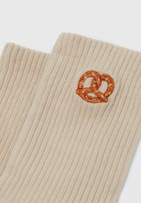 Beige ribbed fabric with an embroidered small orange pretzel design near the edge.