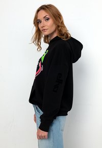 Schwarzer Hoodie mit bunten Grafikdrucken in Grün und Pink. Weicher Stoff, lockerer Schnitt, Kordelzugkapuze und lange Ärmel.
