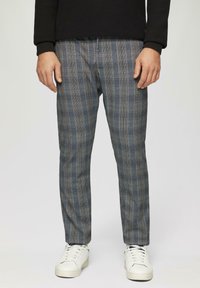Grau karierte Hose mit vertikalen und horizontalen Linien, in taillierter Passform und aus weichem Stoff. Getragen mit weißen Sneakers.