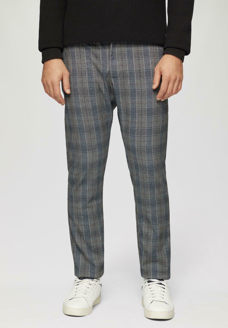 Pantalons à carreaux gris avec des lignes verticales et horizontales, dotés d'une coupe ajustée et d'un tissu doux. Portés avec des baskets blanches.