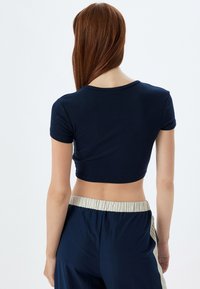 Mørkeblå cropped top med korte ærmer, ribbet tekstur, rund halsudskæring og en tætsiddende pasform, parret med løse mørkeblå bukser med elastisk talje.