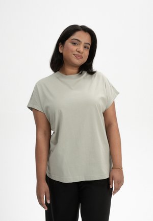 Chemise en coton vert clair avec des manches courtes et un col rond, présentant une coupe décontractée et une texture lisse. Associée à un pantalon noir.