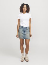 Vit kortärmad t-shirt i kombination med en ljusblå jeanskjol. Skorna är beige sneakers och ljusa strumpor. Enkel design.