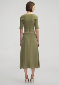 Top en tricot côtelé vert olive à manches courtes et ourlet cropped, associé à une jupe longue assortie en tissu lisse, avec une coupe décontractée.