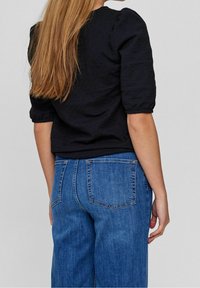 Haut noir texturé à manches bouffantes, associé à un jean en denim bleu taille haute. Présente une coupe décontractée, avec des coutures visibles sur le jean.