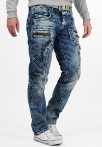 Jeans in denim blu sbiadito con toppe testurizzate, molteplici tasche con zip e branding ricamato sulla coscia sinistra; fit dritto.