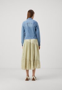 Chaqueta de denim azul claro con un diseño ajustado, combinada con una falda larga y fluida de un patrón verde claro. Zapatos cerrados de color blanco y gris.