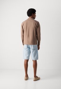 Cămașă maro cu mânecă lungă, pantaloni scurți din denim deschis, pantofi slip-on bej. Material neted, croială lejeră, guler simplu și mâneci cu nasturi.