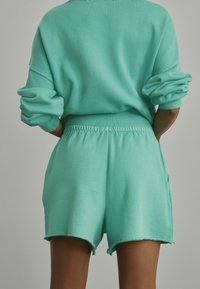 Hanorac oversized de culoare verde mentă cu mâneci răsucite, asociat cu pantaloni scurți cu cordon asortați, având un tiv brut și buzunare laterale.