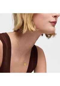 Collana con pendente a forma di orso in oro su una delicata catena, caratterizzata da una finitura liscia. Lo sfondo è neutro, mettendo in risalto i gioielli.