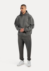 Grauer Kapuzenpullover mit Fronttasche, kombiniert mit passenden schmal zulaufenden Hosen. Weiße Sneakers runden den Look ab. Minimalistisches Design.