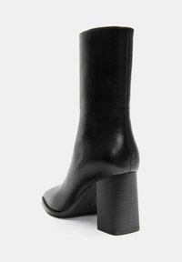Crne kožne čizme do gležnjeva sa četvrtastim vrhom i masivnom blok petom. Glatka tekstura i minimalistički dizajn, bez vidljivih dodataka ili ukrasa.