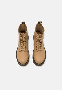 Bottines en cuir beige avec une finition texturée, des bouts ronds, une doublure en tissu et des coutures jaunes le long de la semelle en caoutchouc noire.