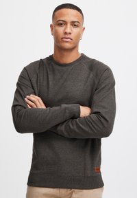Donkergrijs, lange mouwen sweatshirt met ribgebreide manchetten en boord, voorzien van een klein bruin leren logo patch op de linker onderkant. Zachte textuur.