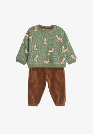 Grünes Langarmhemd mit einem Tigerprint auf einem strukturierten Hintergrund, kombiniert mit braunen Cordhosen mit Taschen und gerippter Textur.