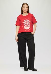 Rode katoenen T-shirt met witte grafische ontwerpen met bloemmotieven en tekst. Gecombineerd met zwarte wijde jeans en zwarte enkellaarsjes.