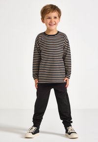 Gestreiftes Langarmhemd in Schwarz und Beige, kombiniert mit schwarzen Jogginghosen mit strukturierten Paneel-Accents und weißen Turnschuhen.