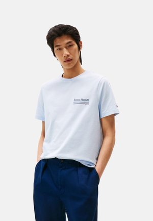 Camiseta de algodón de color azul claro con cuello redondo y mangas cortas. Presenta el logo "TOMMY HILFIGER" en azul más oscuro en la parte izquierda del pecho.