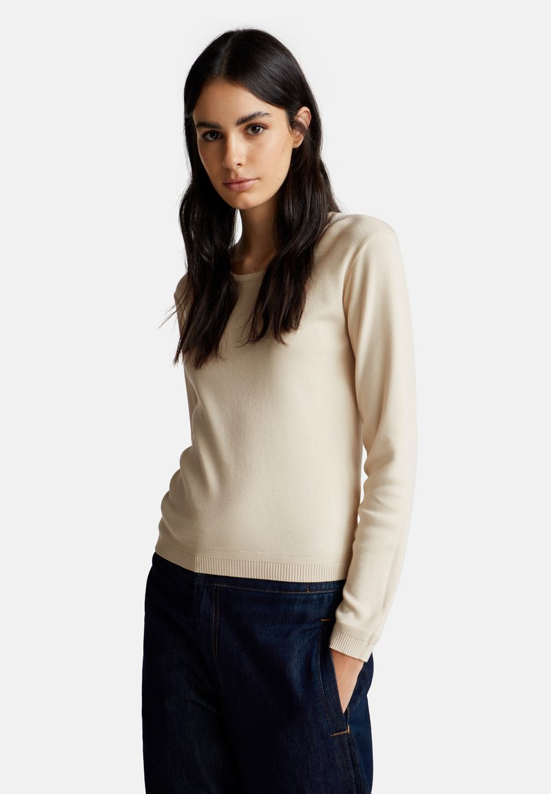 Beige lange mouwen gebreide trui met een ronde hals, geribbelde manchetten en zoom. Gladde textuur, nauwsluitende silhouet, gecombineerd met donkere jeans.