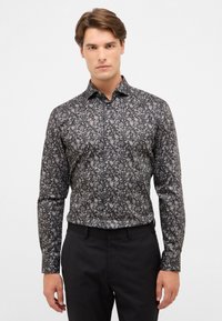 Schwarzhemd mit langen Ärmeln und detailliertem Blumenmuster in Grautönen, mit spitzem Kragen und knöpfbaren Manschetten, kombiniert mit schwarzen Hosen.
